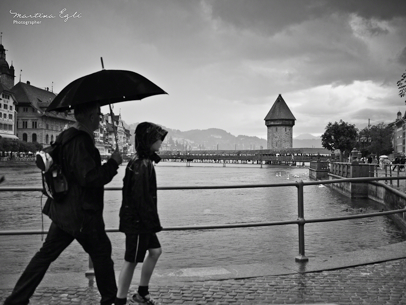 Two people walk with an umbrella past the old bridge in Luzern, Switzerland