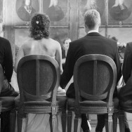 A seated couple undertaking their nuptuals, photographed from behind.