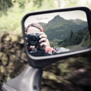 A self portrait reflected in a car wing mirror, a moutain in the background.