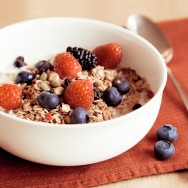 A tasty muesli with raspberries, blueberries and blackberries in a white bowl.