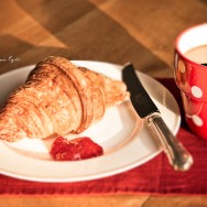 A croissant and some jam on a white plate with a cup of black coffee.