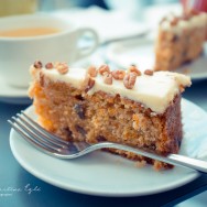 A carrot cake on a white plate with a cup of tea.