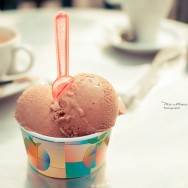 A tub of chocolate ice cream and pink spoon.