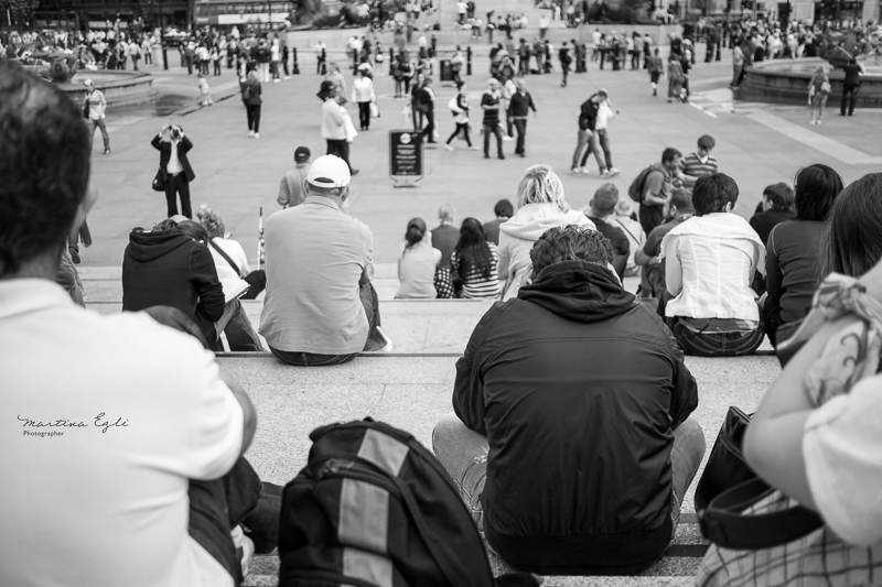 People sitting on the steps of Trafalgar Square in London.