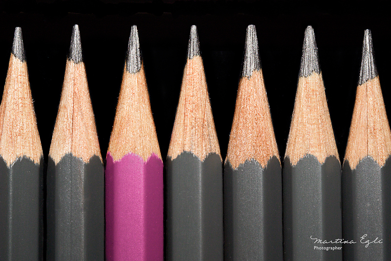 A pink pencil surrounded by grey pencils