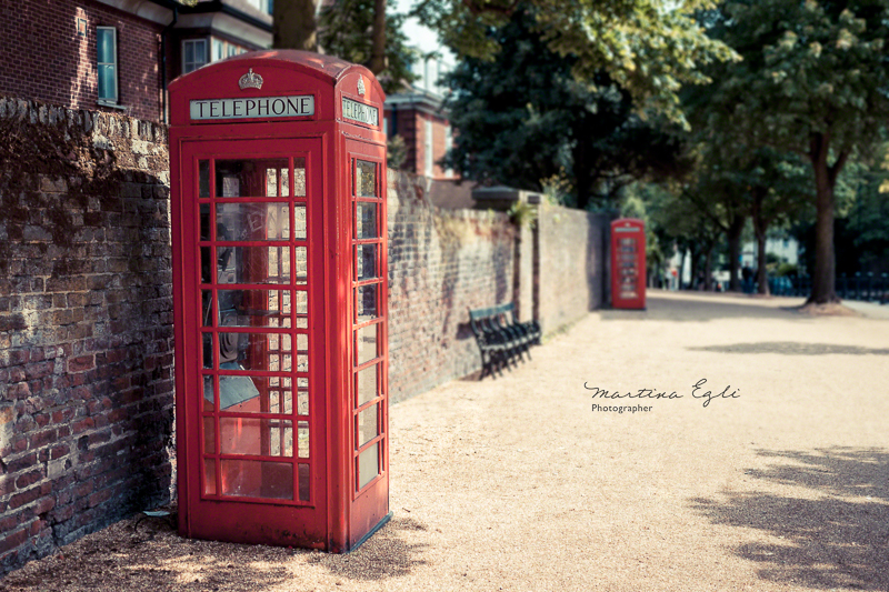 A traditional red phone box in a leafy road in London.