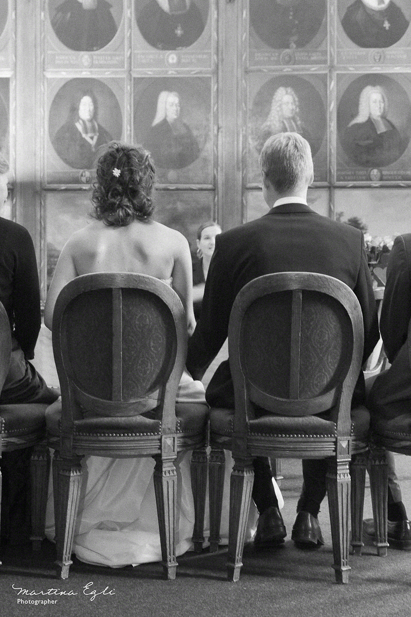 A seated couple undertaking their nuptuals, photographed from behind.