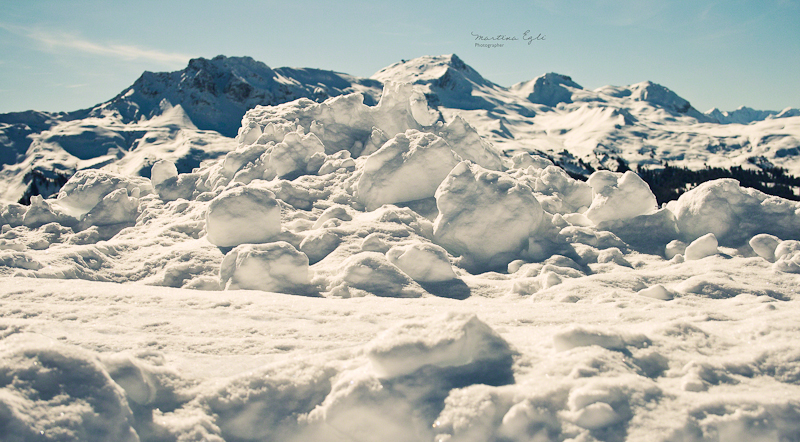 A pile of snow with the Alps in the background.