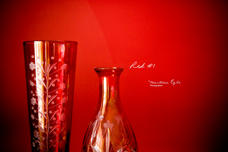 A red vase and a red bottle against a red wall.