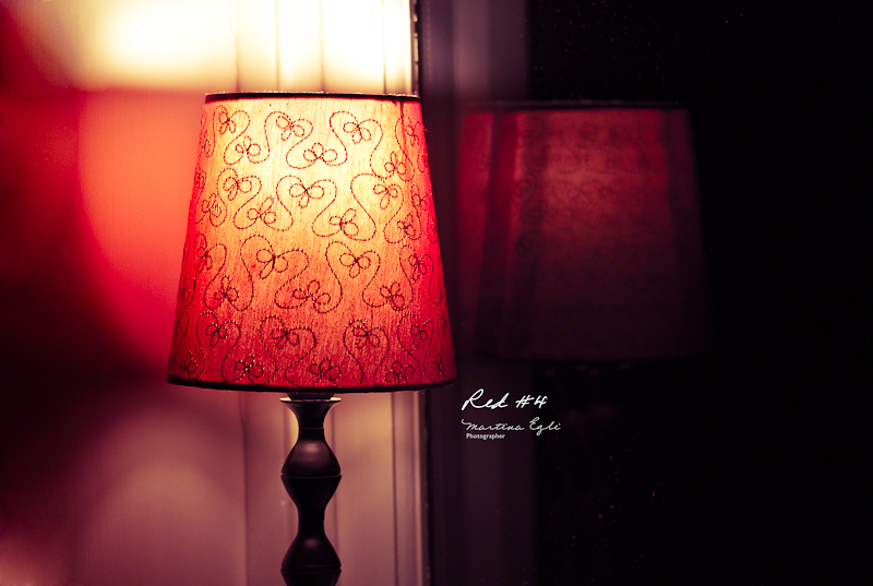 A red table lamp and its reflection in the window.