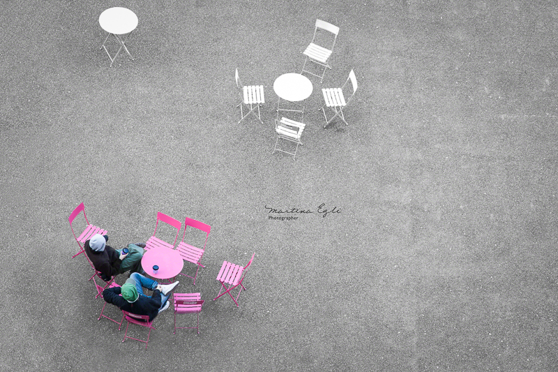 Two men drinking coffee at a pink table taken from a vantage point.