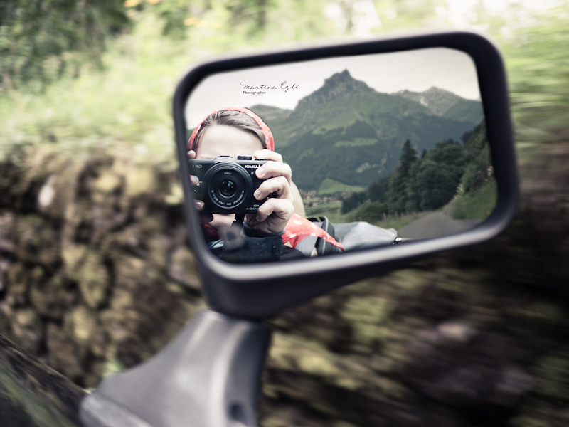 A self portrait reflected in a car wing mirror, a moutain in the background.