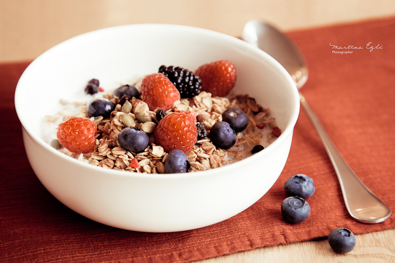 A tasty muesli with raspberries, blueberries and blackberries in a white bowl.