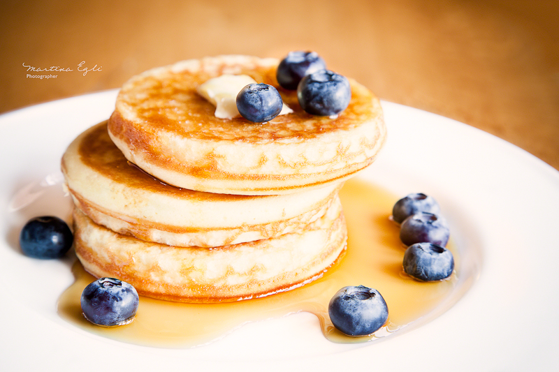 American pancakes with maple syrup and bluerberries on a white plate.