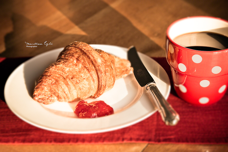 A croissant and some jam on a white plate with a cup of black coffee.