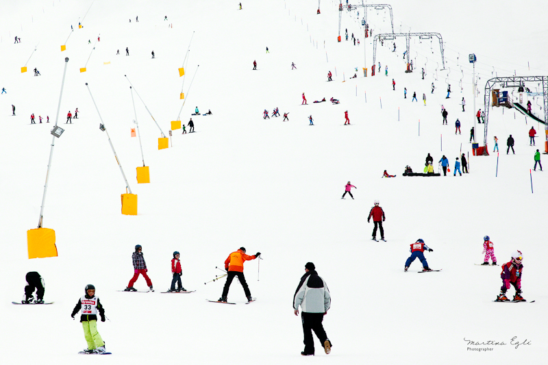 A ski slope in Switzerland full of skiers and snowboarders in colourful clothes.