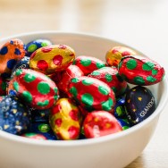 Colourful chocolate Easter Eggs sit in white bowl.