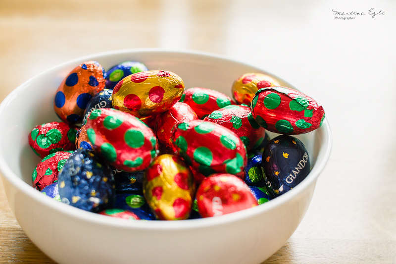 Colourful chocolate Easter Eggs sit in white bowl.