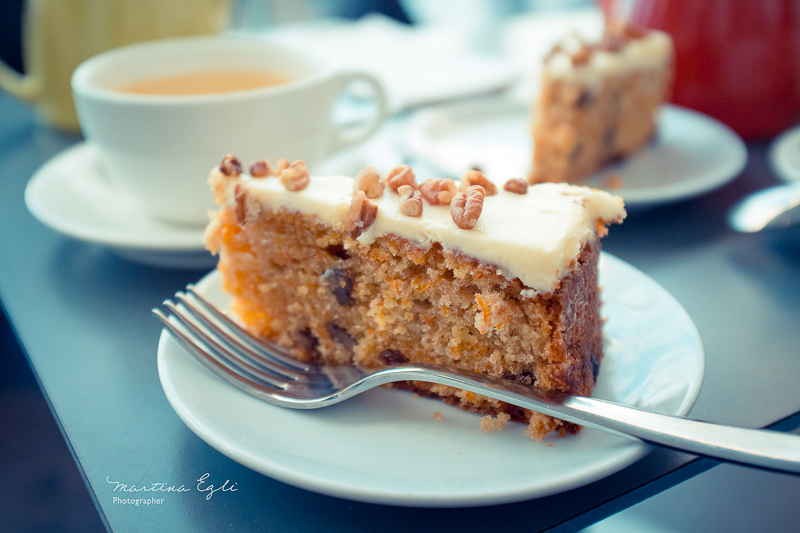 A carrot cake on a white plate with a cup of tea.