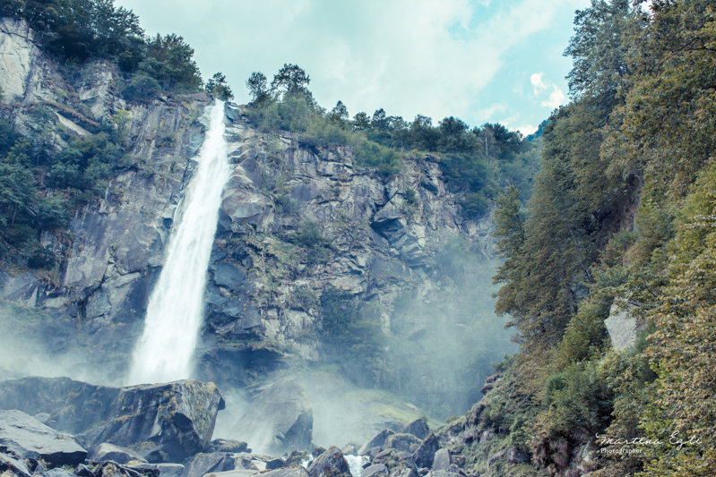 Water cascades down a rock face, mist rises from the base of the waterfall.