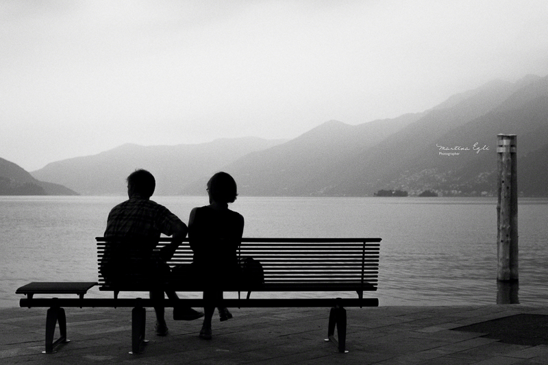 Two people sitting on a bench looking over a lake.